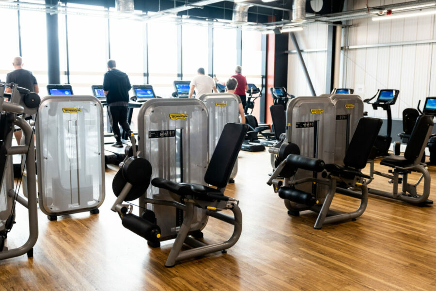 Empty leg extension machines in the foreground with people using treadmills in the background