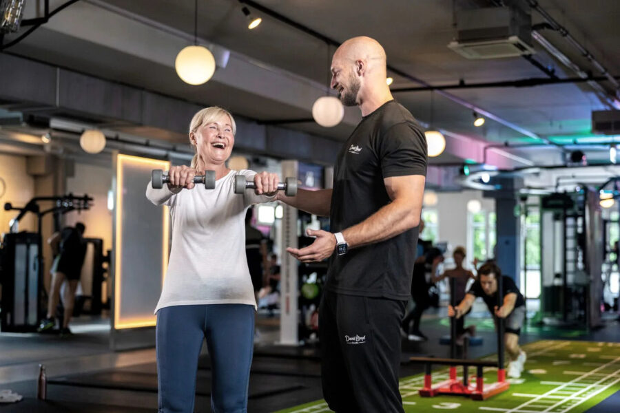 PT helping female perform dumbbell front raises