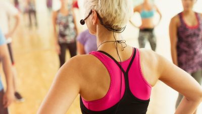 Fitness instructor leading a high-energy group exercise-to-music class with choreography and upbeat music in a modern UK gym studio.