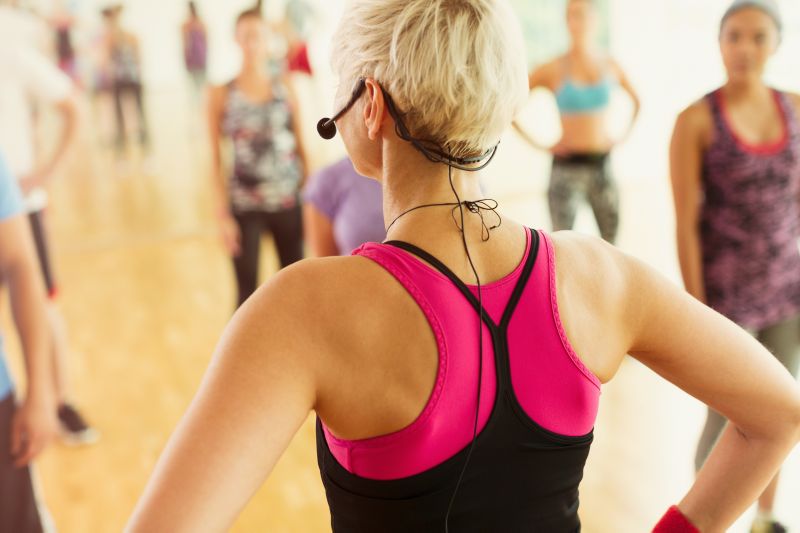 Fitness instructor leading a high-energy group exercise-to-music class with choreography and upbeat music in a modern UK gym studio.