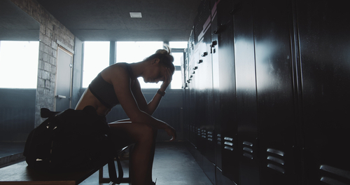 A woman in a gym locker room taking a reflective moment, representing the emotional impact and motivation challenges of Blue Monday.